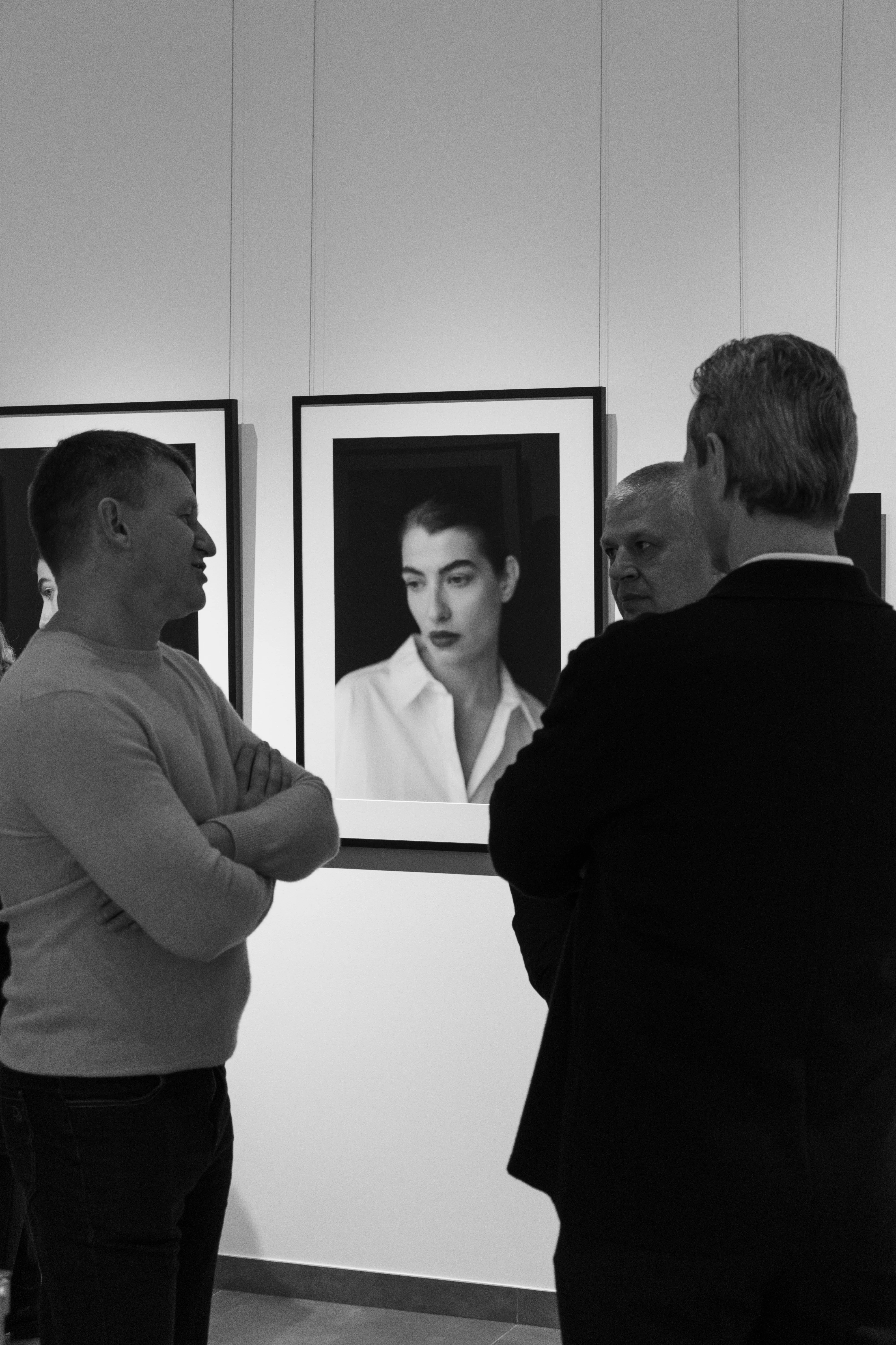 Two men conversing at gallery with portrait photography