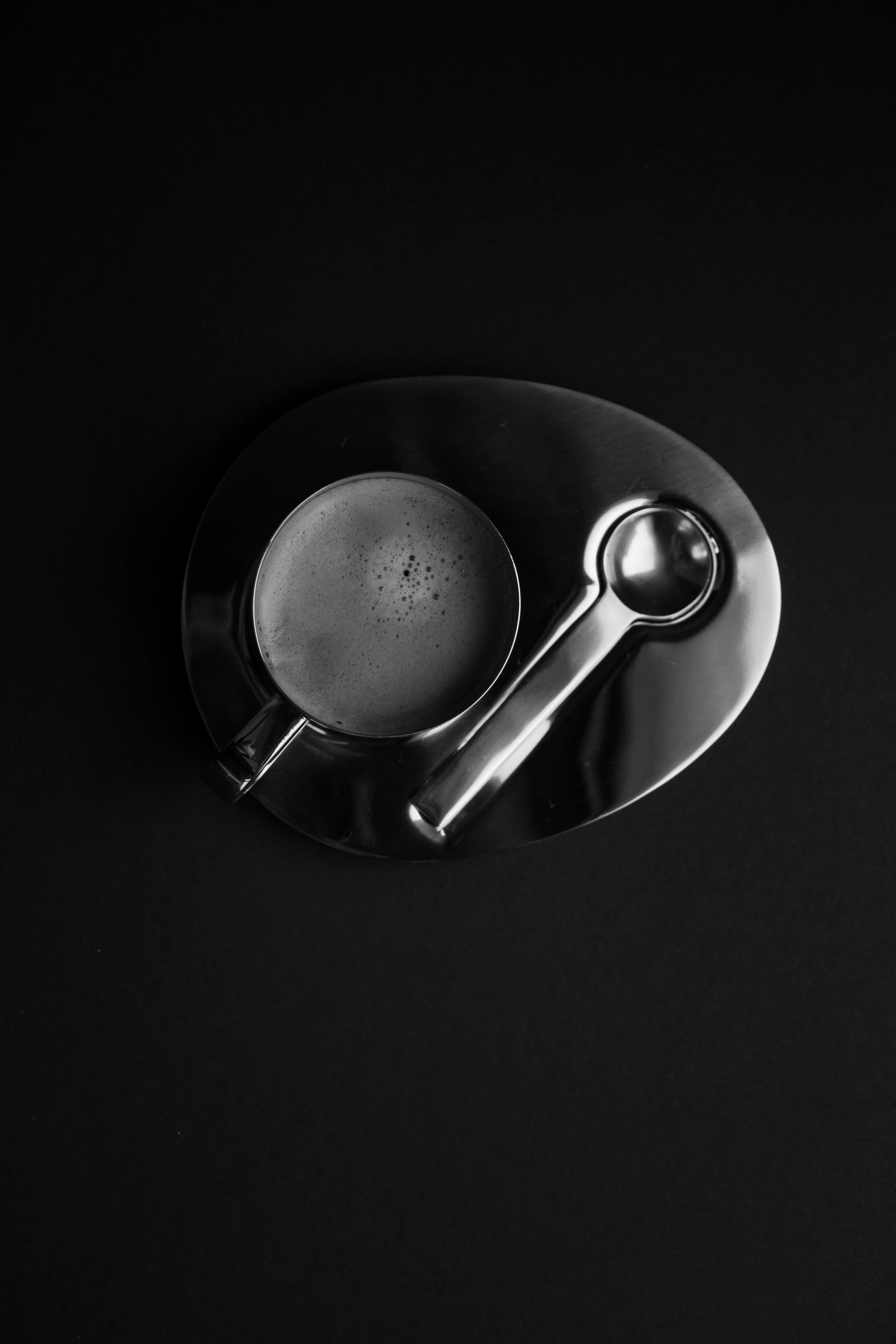 Coffee cup with spoon on dark tray from above