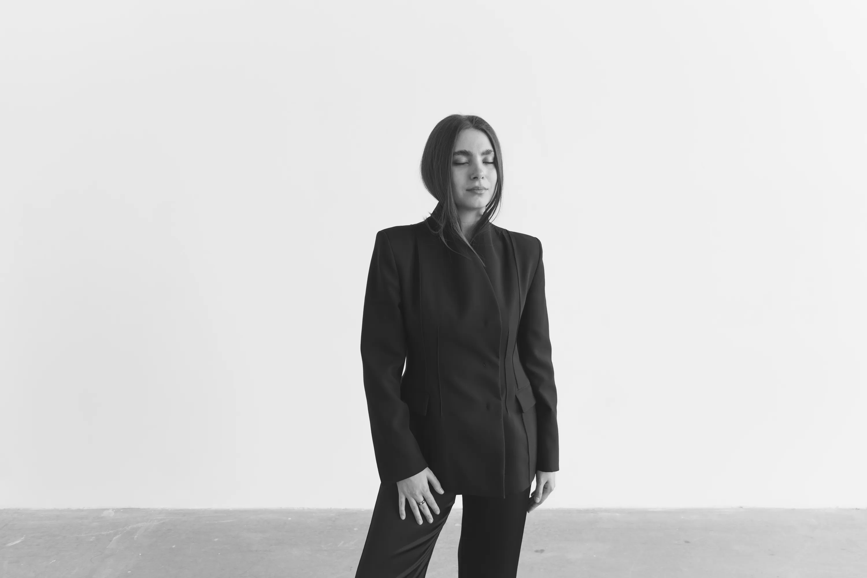 Woman in black suit standing against white wall